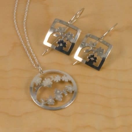 A pair of silver earrings accompanied by a stunning Sendai Blossom Pendant necklace adorned with flowers.
