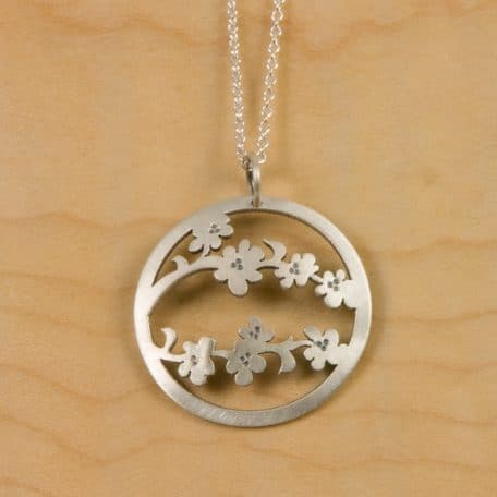 A silver necklace adorned with a Sendai Blossom Pendant featuring an elegant flower centerpiece.
